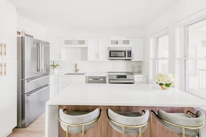 Una cocina moderna con armarios blancos, electrodomésticos de acero inoxidable y una isla central con taburetes de bar.
