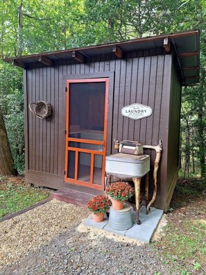 Una pequeña cabaña de madera con una puerta, un cartel que dice 'LAUNDRY' y una mesa rústica con flores.