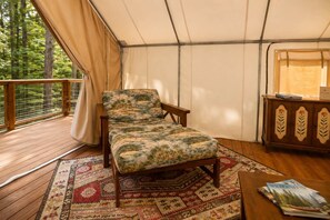 A tented room with a bed, a wooden bench, a table with books, and a view of trees. - Glamorous Glamping Tent w/ A/C & Lodge Access Near Ocoee (Copperhill)