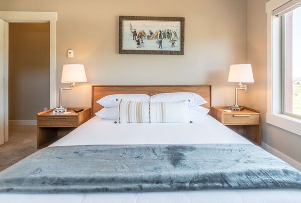 A neatly made bed with a gray blanket, two bedside lamps, and a framed picture on the wall.