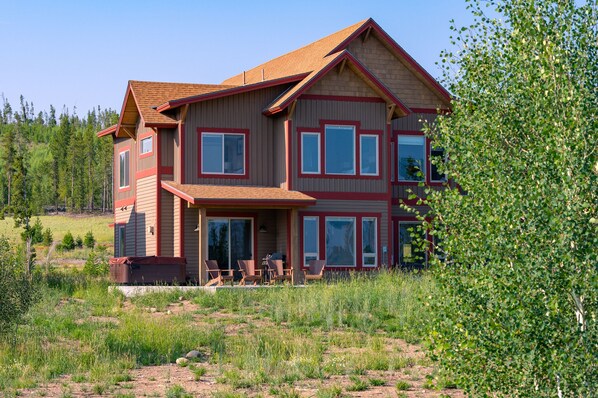 A two-story house with a red and beige exterior, large windows, and a front porch with outdoor seating.