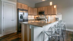 Une cuisine moderne avec des meubles en bois, des appareils en acier inoxydable et un îlot central doté de tabourets de bar.
