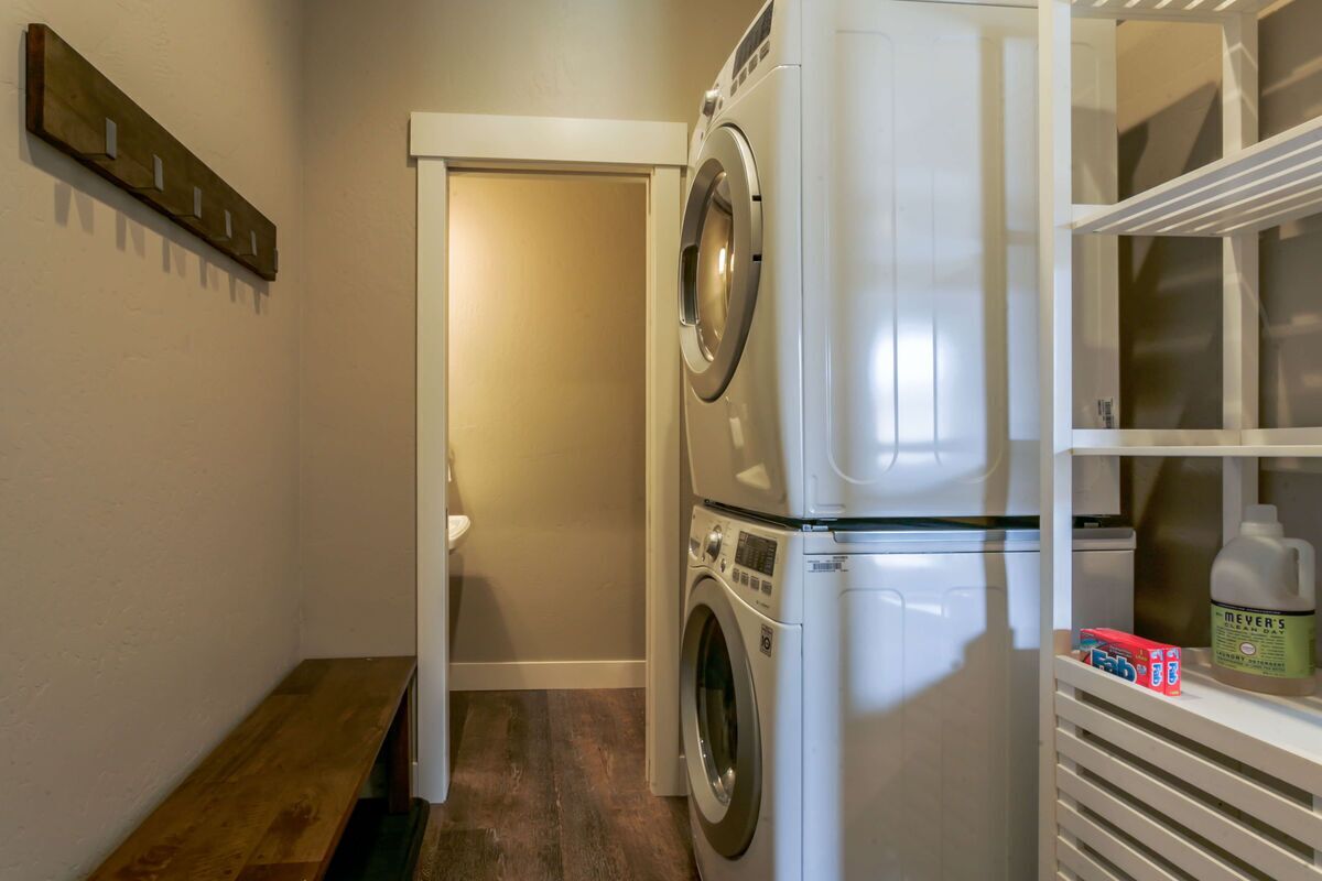 A laundry room with a washing machine, a bench, and a shelf with a detergent bottle.