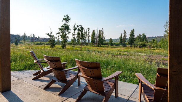 Une terrasse avec quatre chaises en bois donnant sur un champ verdoyant et des arbres, le tout sous un ciel dégagé.
