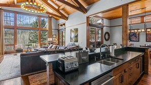 Cocina amplia con una isla grande, vigas de madera y ventanas que dan a vistas de árboles.