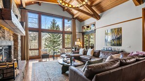 Un salón espacioso con chimenea, sofá de cuero y grandes ventanales con vistas a árboles.