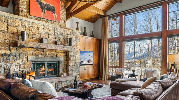 Una sala de estar acogedora con chimenea de piedra, sofás de cuero y un ventanal con vistas a la montaña.