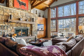 A cozy living room with a stone fireplace, leather sofas, and a large window offering a mountain view.
