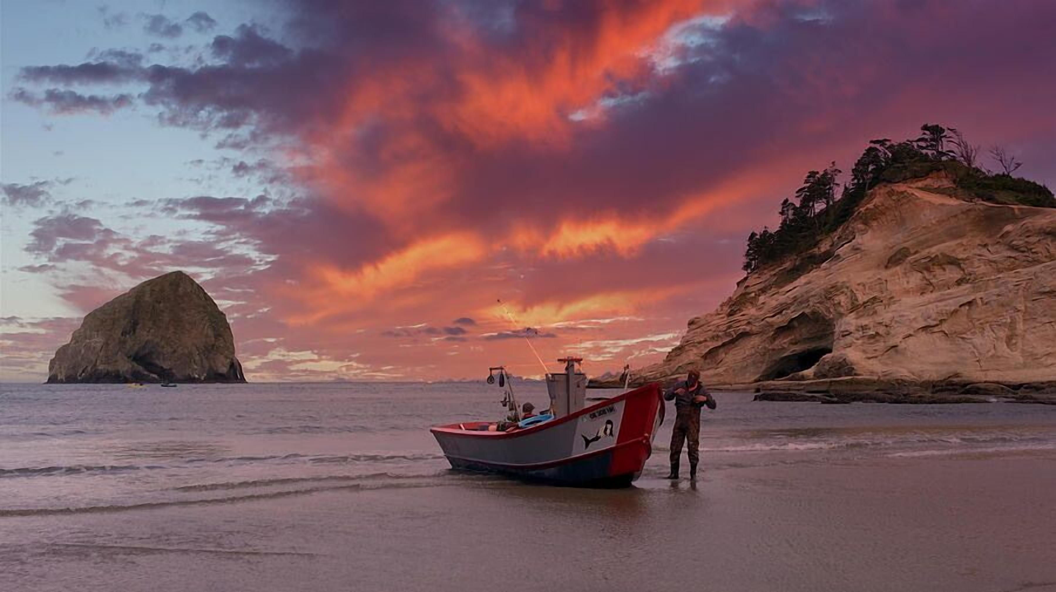 A boat on a beach with a rocky cliff and a large rock formation in the background.