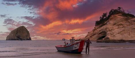 A boat on a beach with a rocky cliff and a large rock formation in the background.