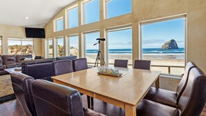 A spacious living area with a large wooden table and leather seating, overlooking a beach with a rock formation.