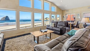 A living room with large windows overlooking a beach, a leather sofa, a coffee table, and a dining area.