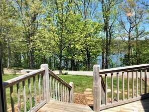 Una terraza de madera que da a una zona cubierta de césped, con un lago y árboles al fondo.