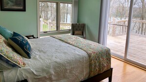 A bedroom with a large bed, two windows, a chair, and a view of a deck. - Beautiful Vacation Home on Lake Cumberland, Monticello, KY (Monticello)