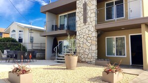 A modern two-story building with a stone facade, outdoor seating, and potted plants.