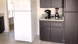 A kitchen with a white refrigerator, dark cabinets, a coffee maker, and a blender.