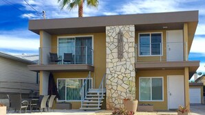 A two-story modern house with a stone facade, a balcony, and a palm tree.