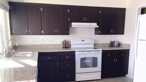 A kitchen with dark cabinets, a white stove, and a sink.