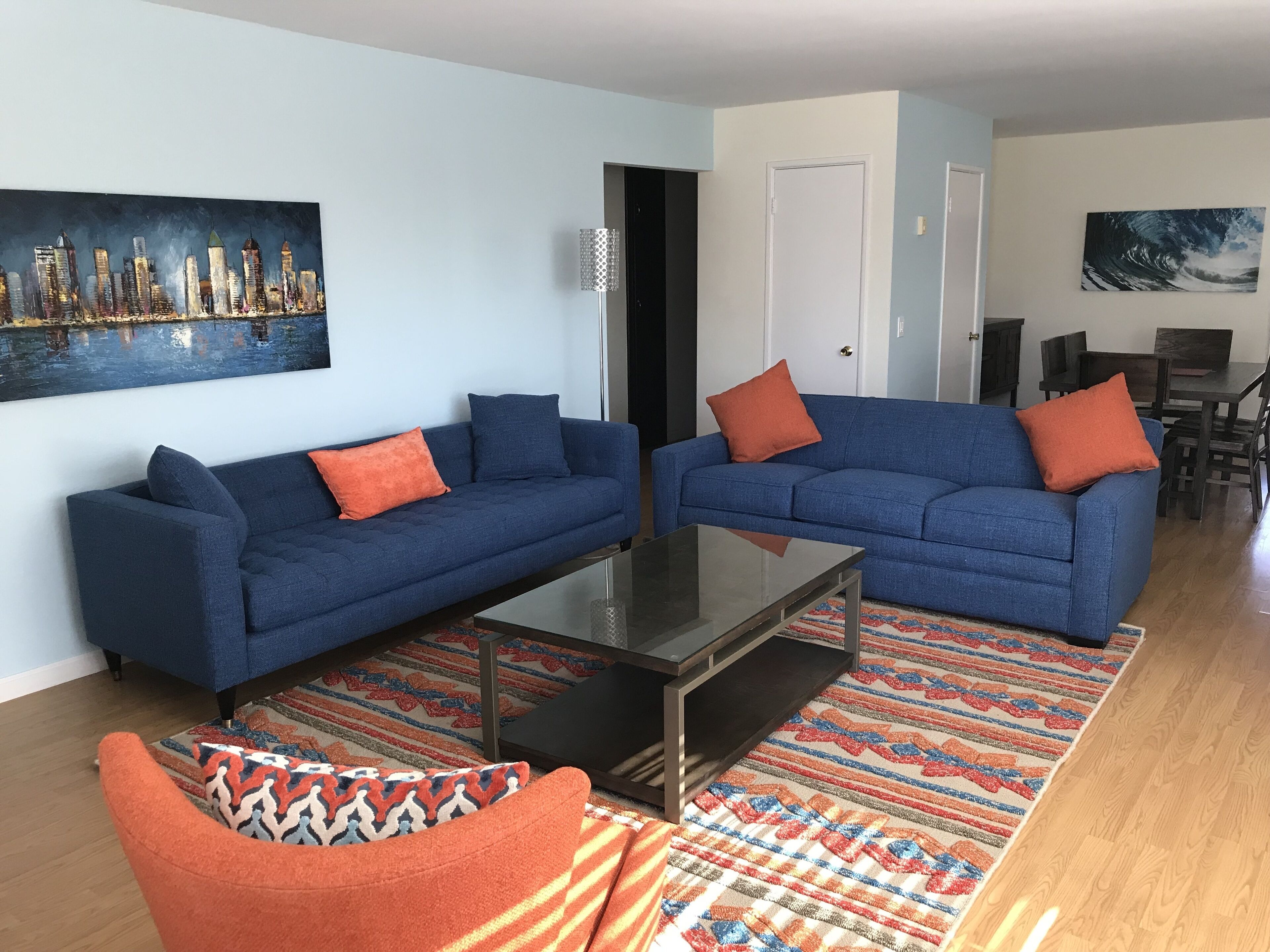A living room with two blue sofas, a glass coffee table, and a colorful rug.
