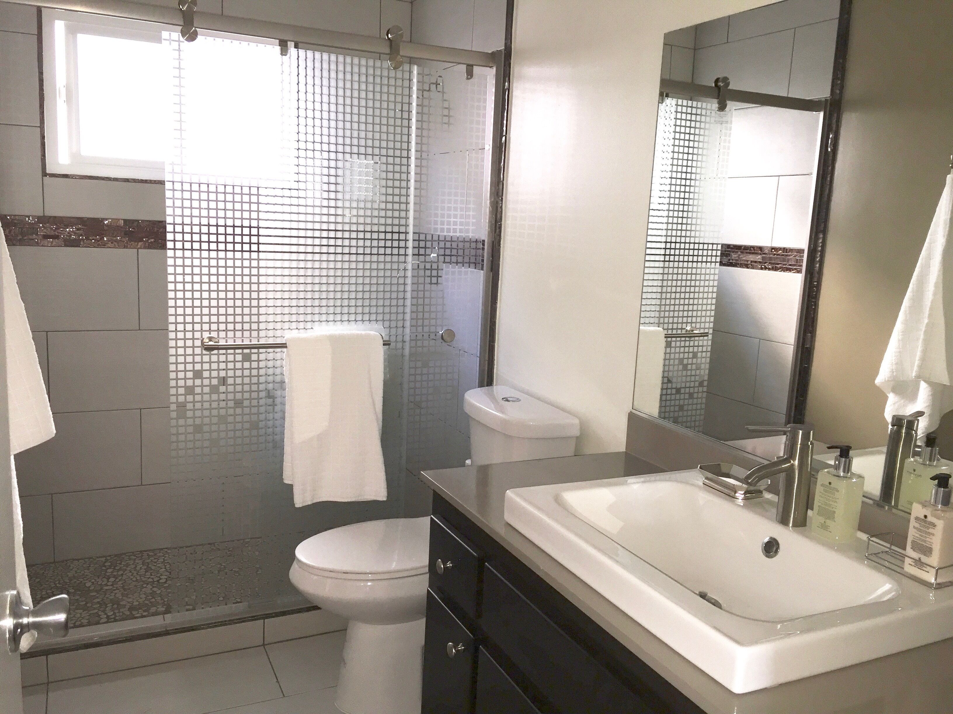 A modern bathroom with a glass shower enclosure, a white toilet, and a large sink with a mirror above it.