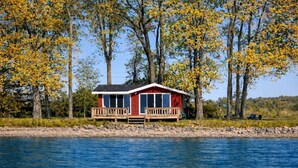 Una cabaña con terraza, ubicada a orillas de un lago con árboles al fondo.