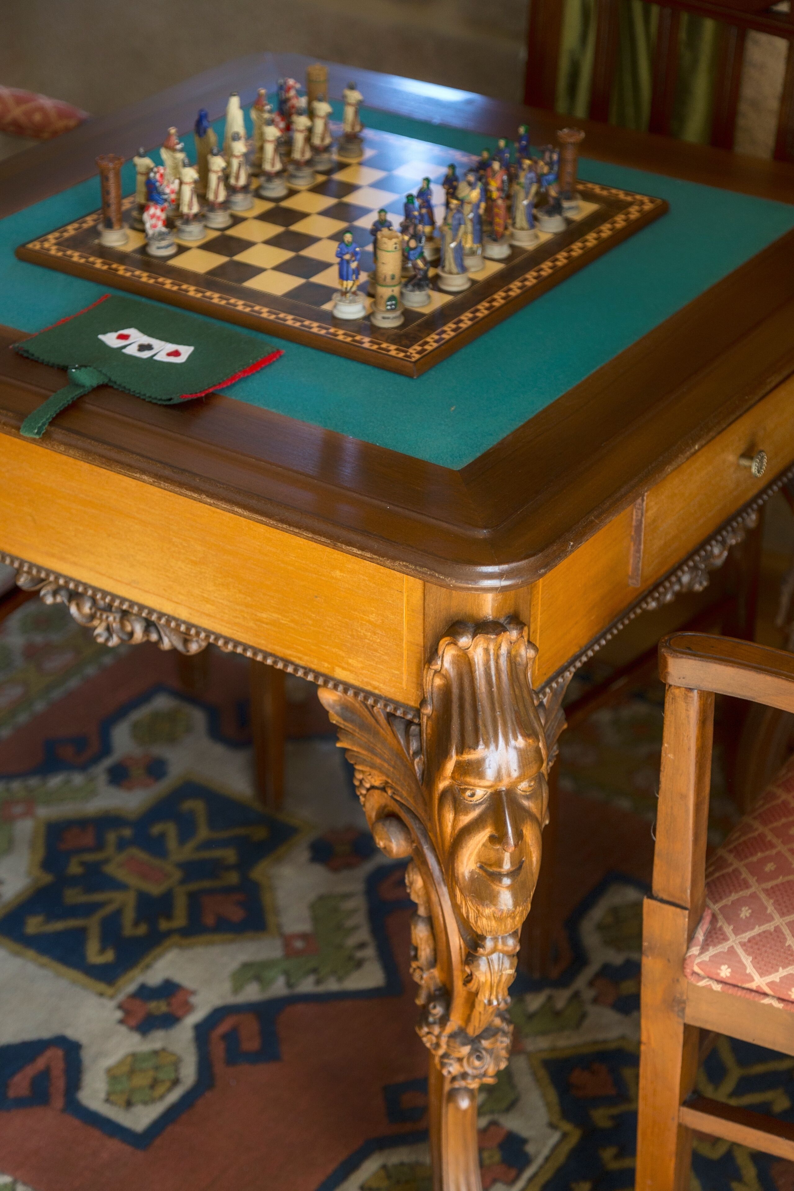 Un tablero de ajedrez sobre una mesa de madera con intrincados grabados, sobre una alfombra estampada.