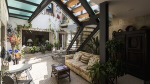 Un espacio interior amplio con techo alto, una escalera y diferentes distribuciones de asientos, incluyendo un sofá y sillas.