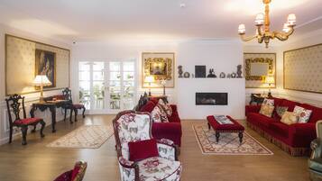 A spacious living room with a red sofa set, a floral armchair, and a chandelier.