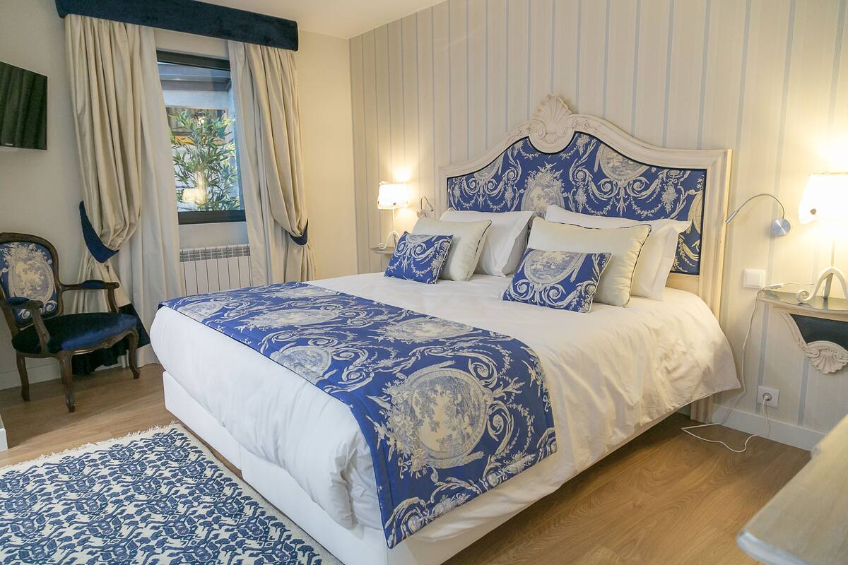 A bedroom with a large bed, a chair, a nightstand, and a window with curtains.