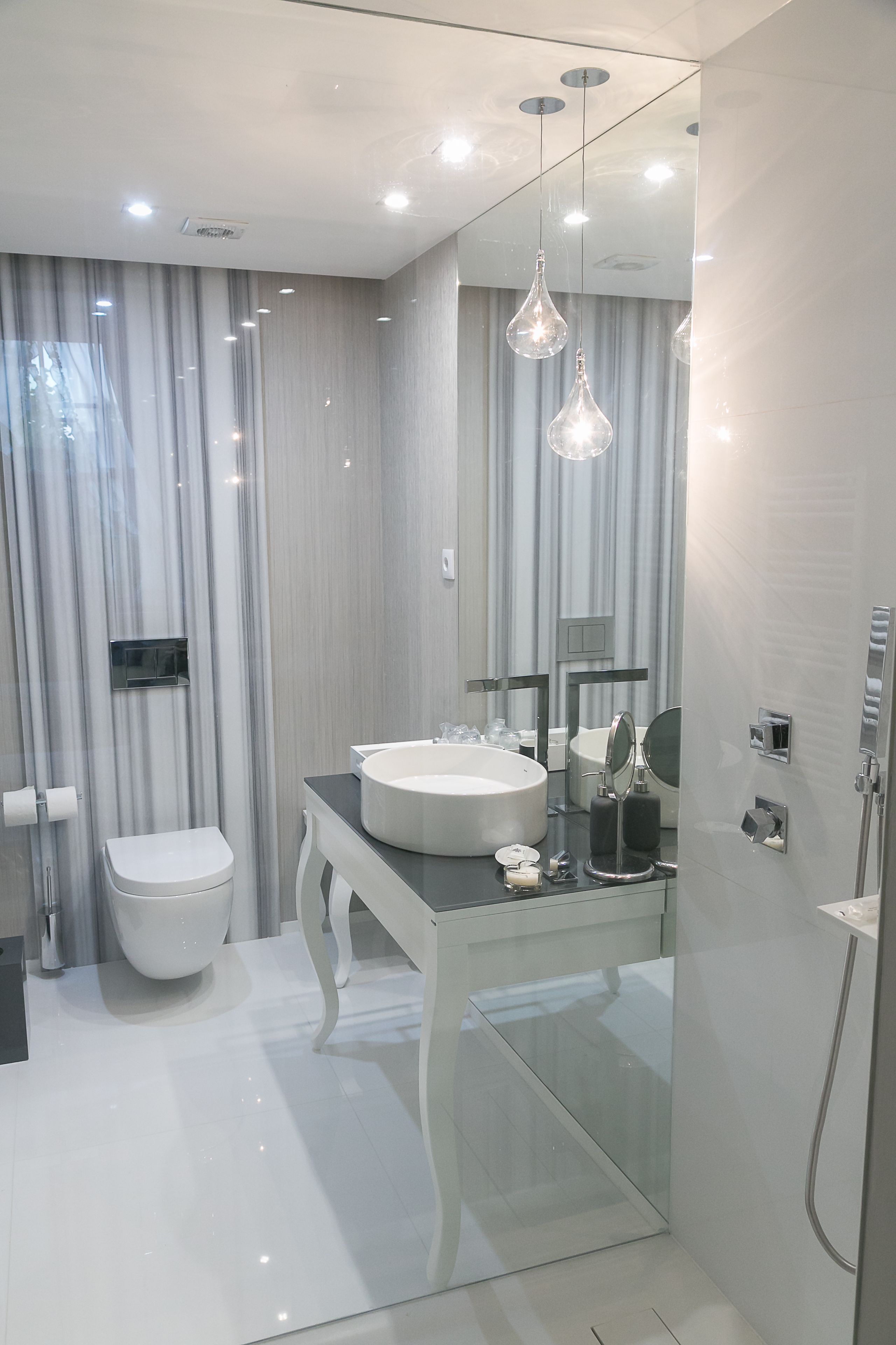 Un baño moderno con cabina de ducha de vidrio, un lavamanos blanco y un tocador con espejo.