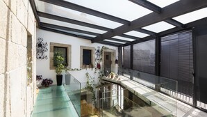 Un interior moderno con una escalera de cristal, una pared blanca con detalles de metal decorativo y un ventanal con contraventanas negras.