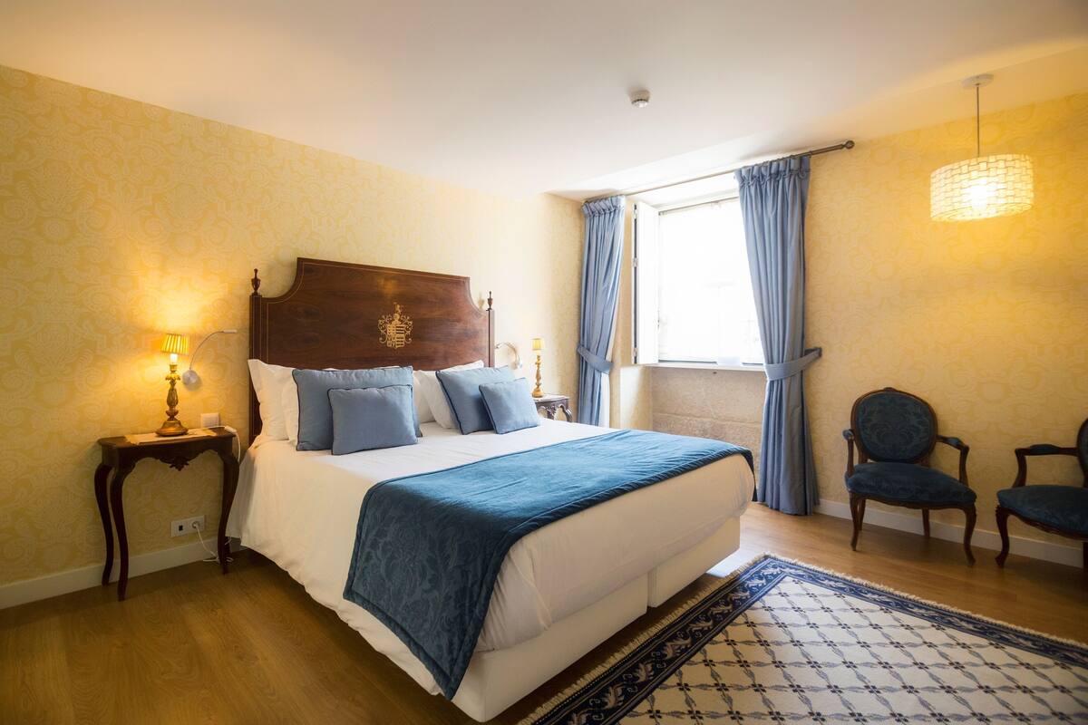 A bedroom with a large bed, two bedside tables, a window with curtains, and two chairs.