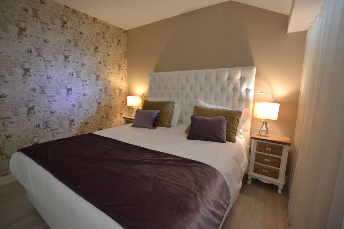 A bedroom with a large bed, two bedside tables, and a patterned wallpaper.