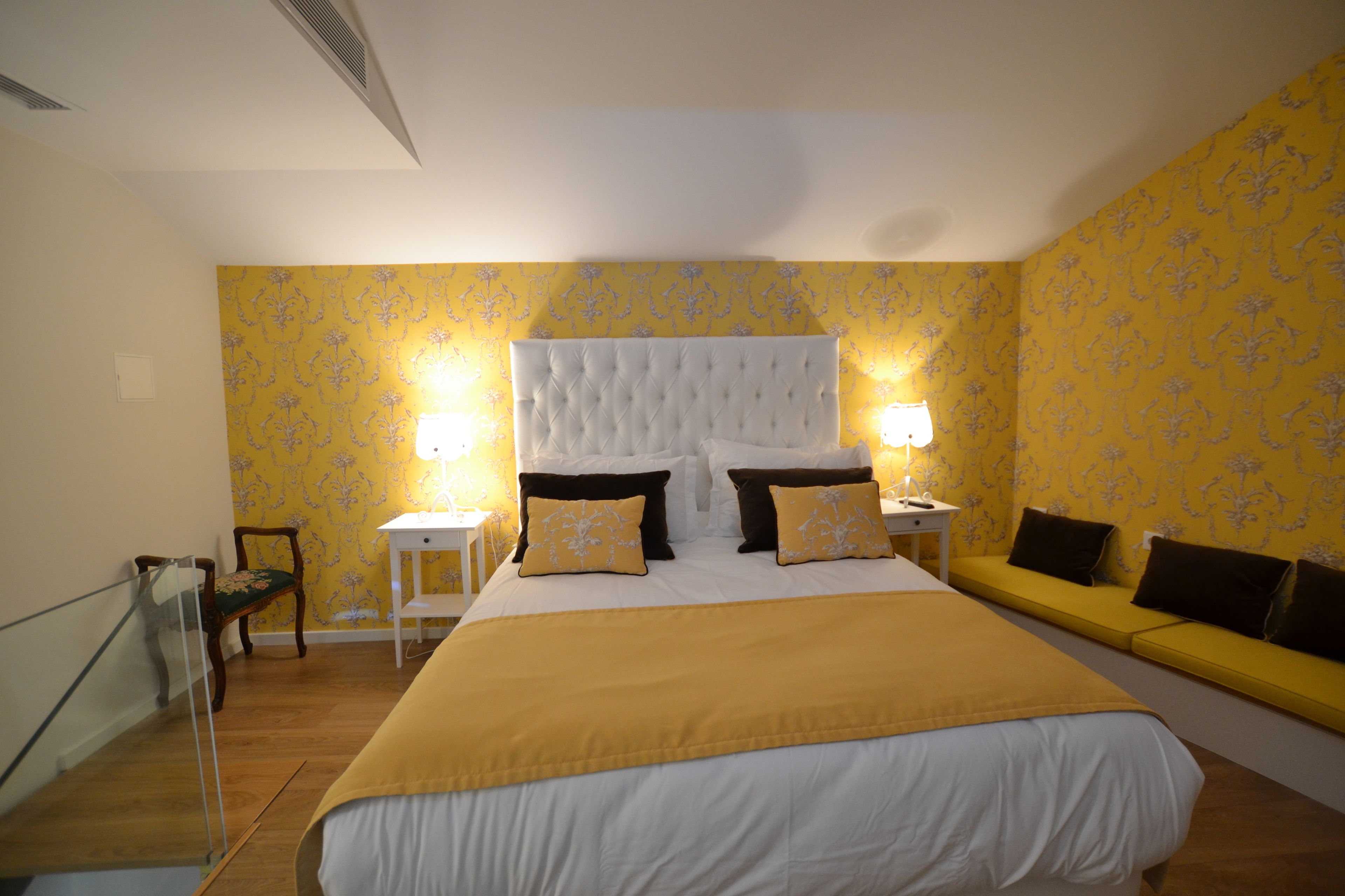 Une chambre à coucher avec un grand lit, deux tables de chevet avec des lampes, un banc le long du mur et un plancher en bois.