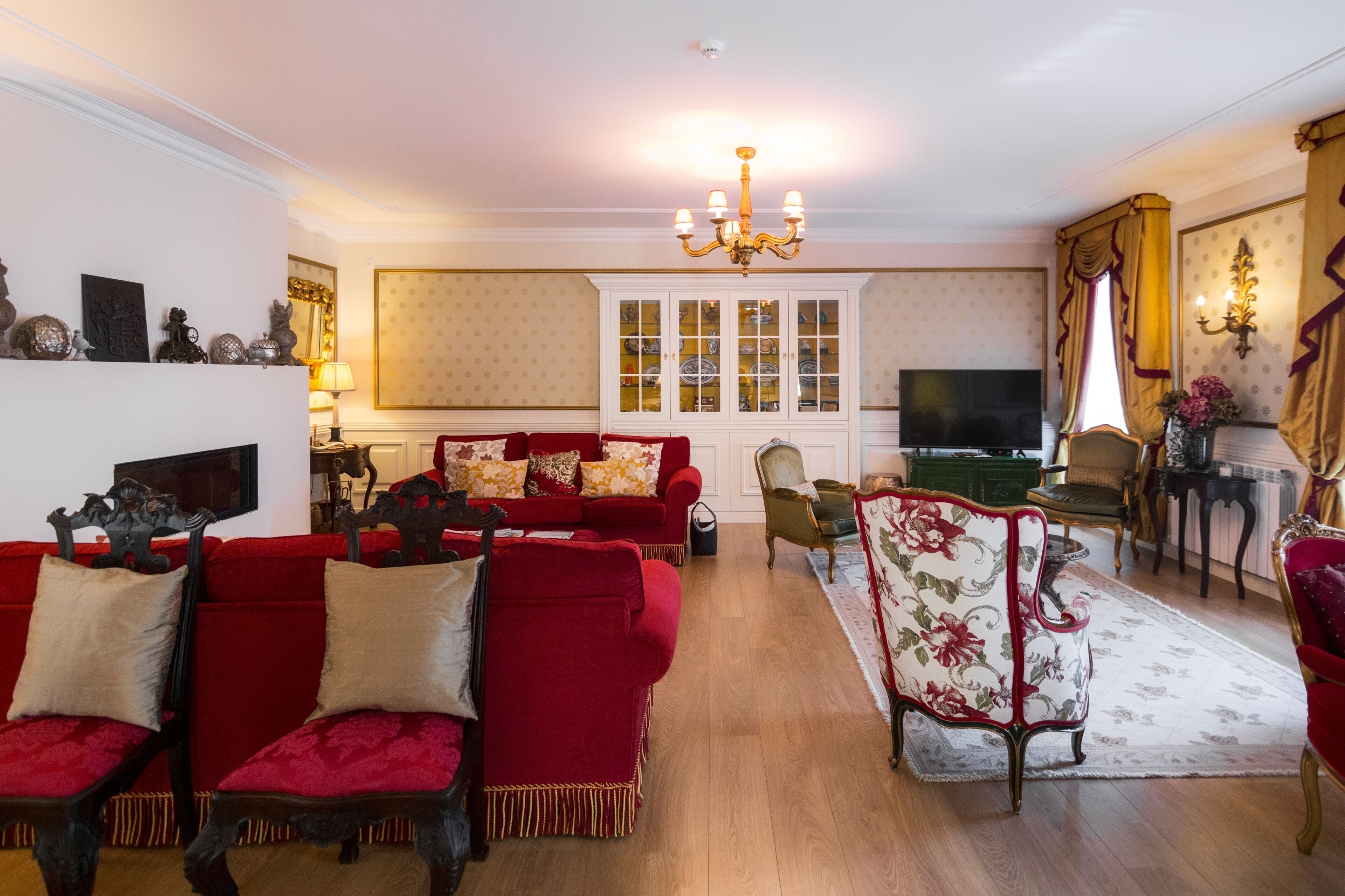 A traditional living room with a red sofa set, a chandelier, and a television.
