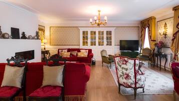 A traditional living room with a red sofa set, a chandelier, and a television.
