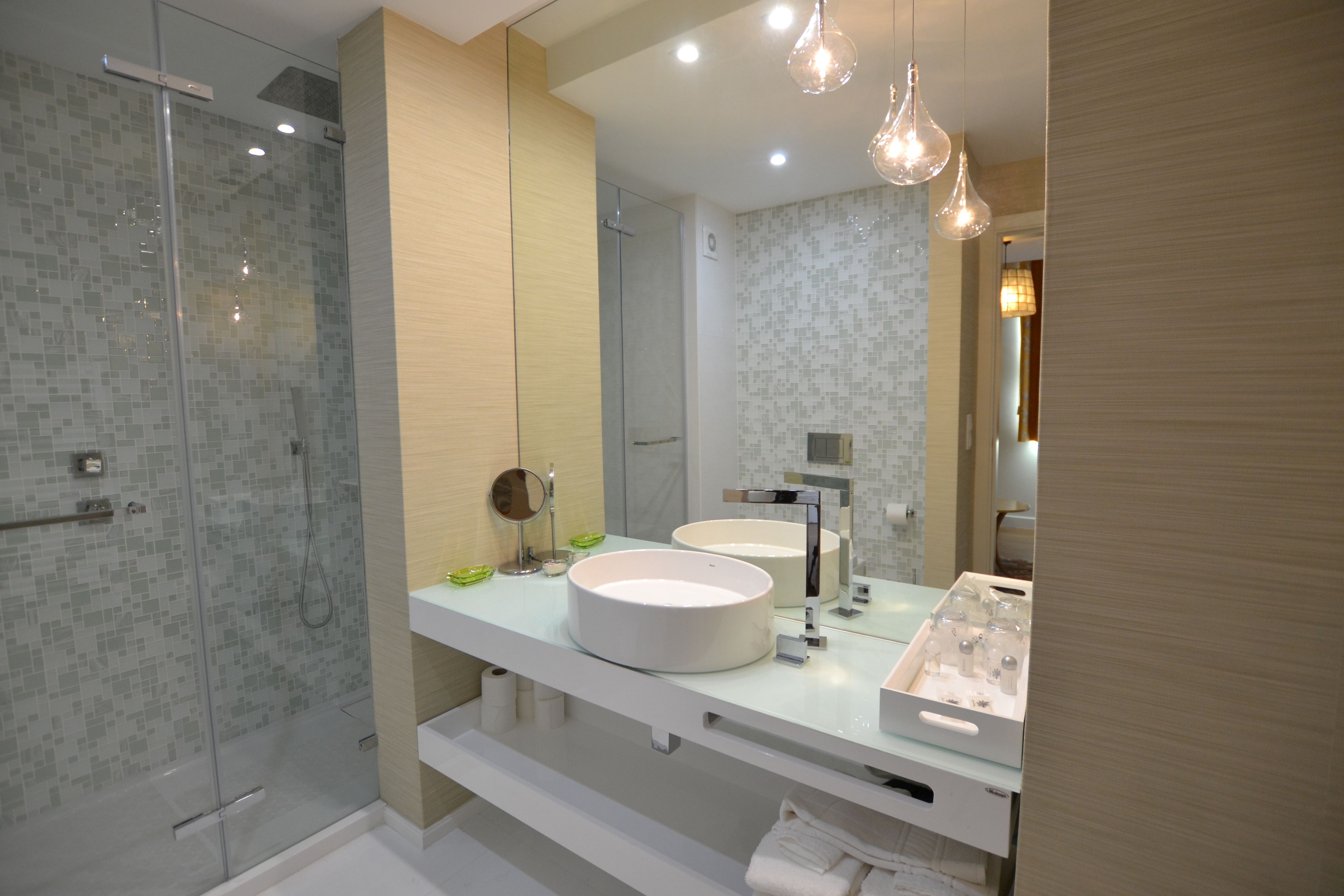 Un baño moderno con ducha de vidrio, dos lavamanos y un espejo grande.