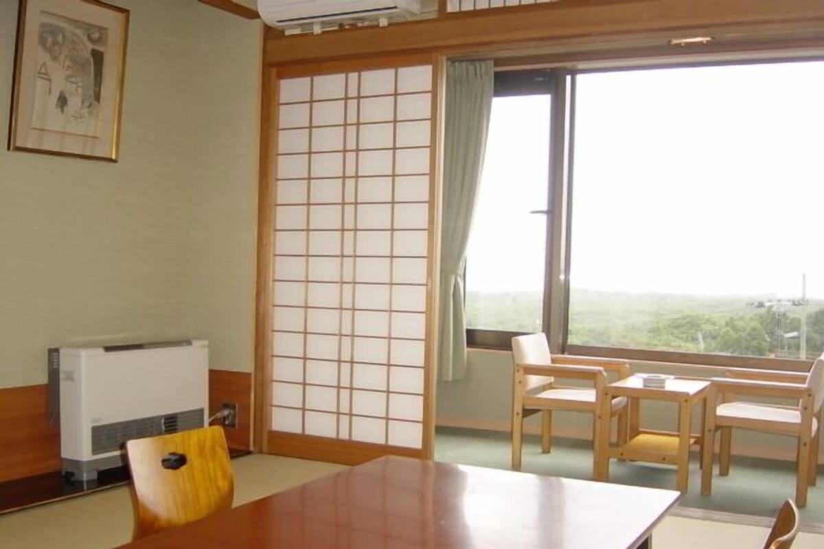 A traditional Japanese room with tatami flooring, a low table, wooden chairs, a shoji screen, and a view through a large window.