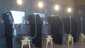 Una fila de cabinas de ducha con taburetes de madera, suelo de baldosas e iluminación en el techo.