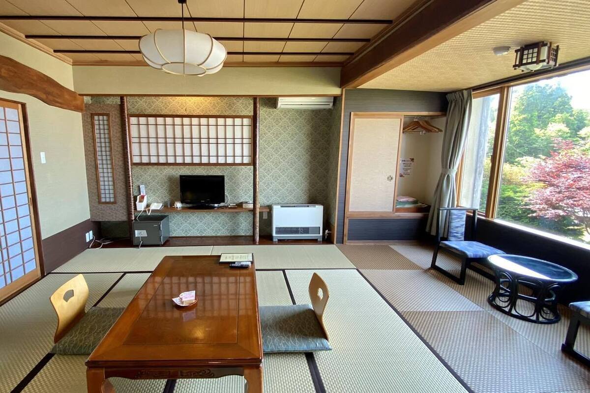 A traditional Japanese room with tatami flooring, a low table with cushions, a television, and a sliding door.