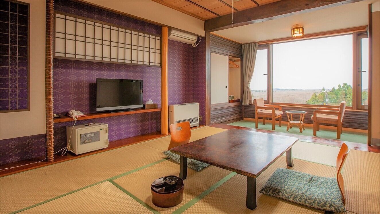 A traditional Japanese room with tatami flooring, a television, a heater, a table, and chairs.
