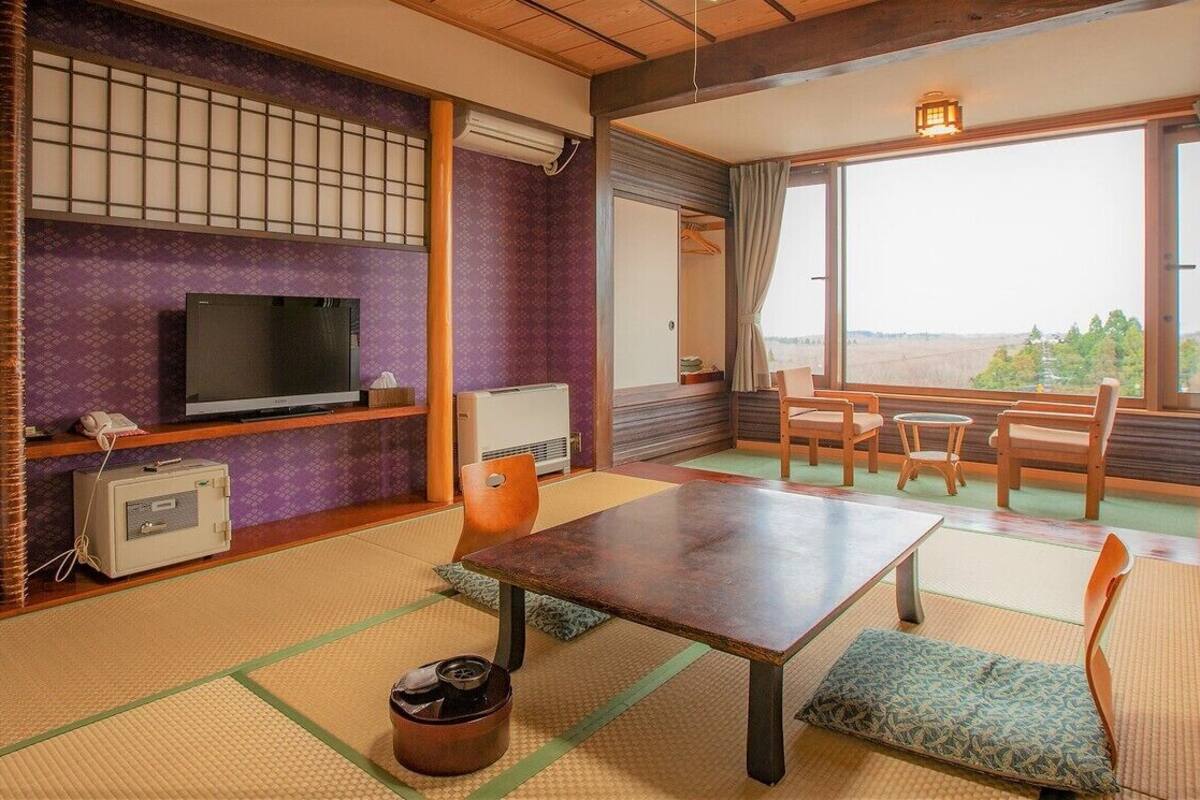 A traditional Japanese room with tatami flooring, a television, a heater, a table, and chairs.
