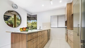Una cocina moderna con armarios de madera, una isla grande con fruta, un espejo redondo y un ventanal con persianas.