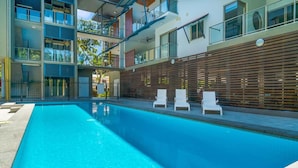 Un edificio moderno con piscina, sillas de descanso y una valla de madera.