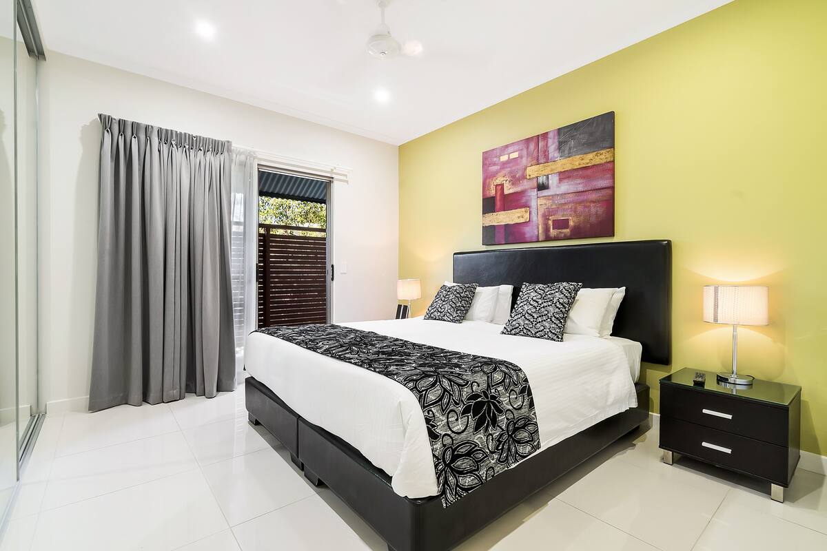 A bedroom with a bed, a nightstand, a lamp, and a window with curtains.
