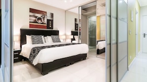Un dormitorio moderno con una cama grande, mesitas de noche, un box de ducha de vidrio y una puerta corrediza de vidrio que da al baño.