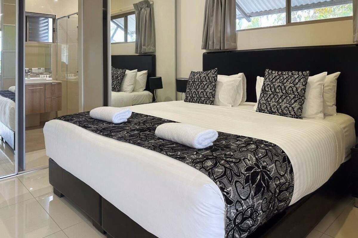 A modern hotel room with a large bed, a glass shower area, and a view of the outdoors.
