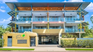 Un hotel de varios pisos con diseño moderno, que cuenta con balcones, un estacionamiento techado y un letrero que indica el nombre y la ubicación.
