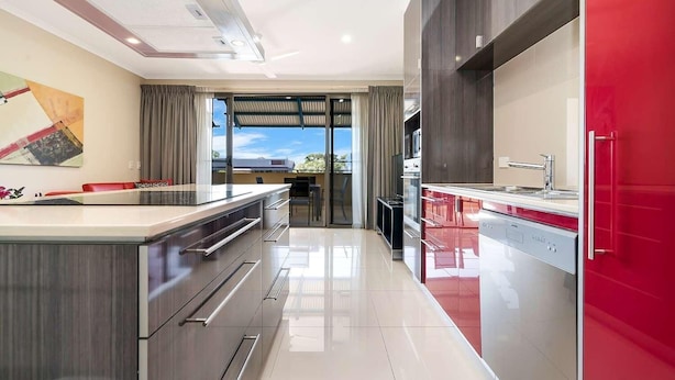 Una cocina moderna con una isla grande, una pared de acento roja y vistas al exterior.