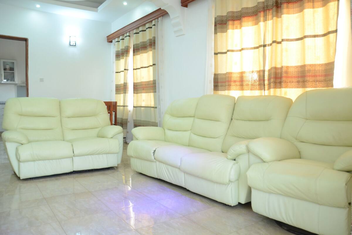 A living room with two cream-colored sofas, a wooden coffee table, and a large window with patterned curtains.